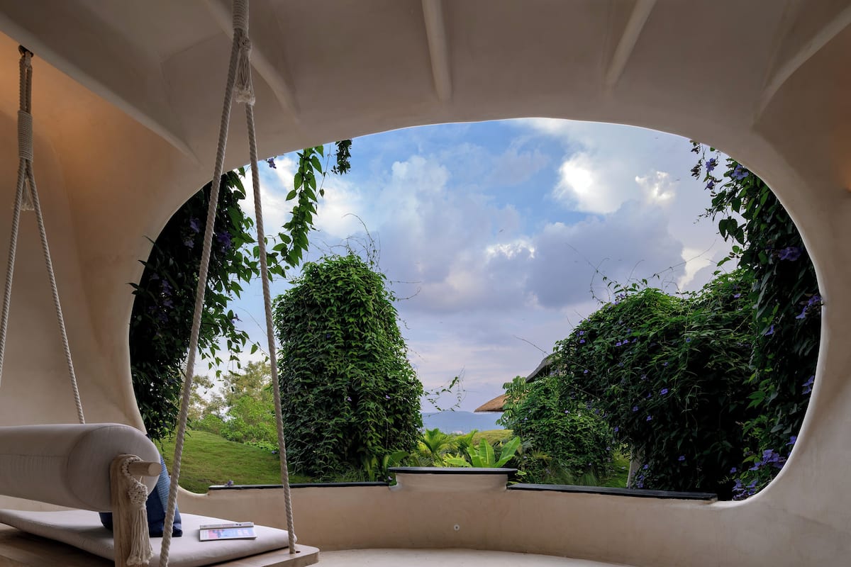 Ein Zimmer mit einem großen, ovalen Fenster, einer Schaukel und Blick auf Grünflächen und ein Gebäude.