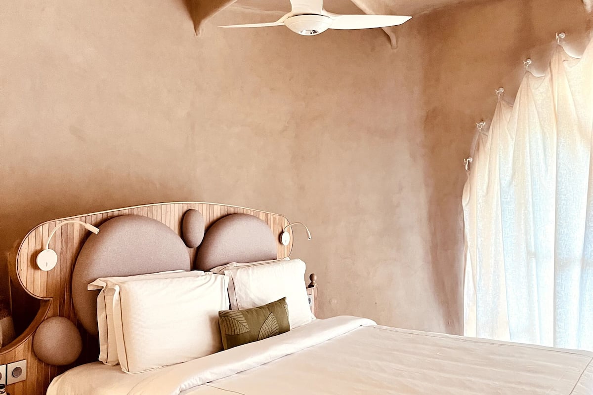 Ein Schlafzimmer mit einem Bett, einem Deckenventilator, einem Holzkopfende und einem Nachttisch.