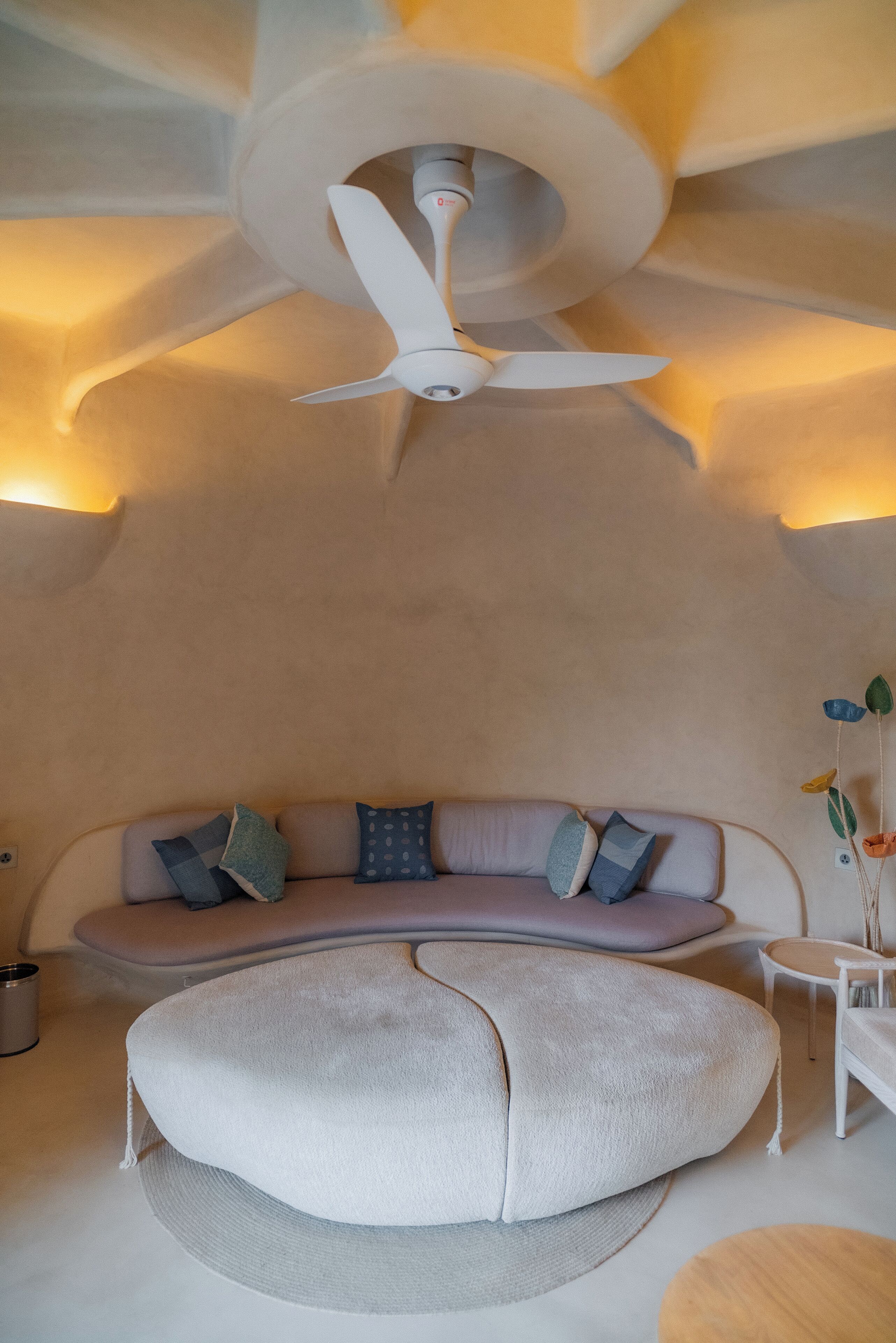 A modern interior with a ceiling fan, a sofa with patterned cushions, and a round ottoman.