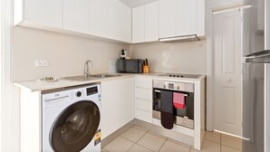 A compact kitchen with white cabinets, a built-in washing machine, a microwave, an oven, and a stainless steel refrigerator. - Bright 3-bed Apartment Near Coogee Beach (Sydney)