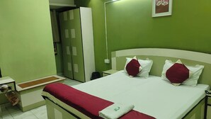 Un letto ben rifatto con copriletto rosso e bianco, un cuscino bianco e un cuscino rosso. Sul muro verde è appesa una cornice con un'immagine.
