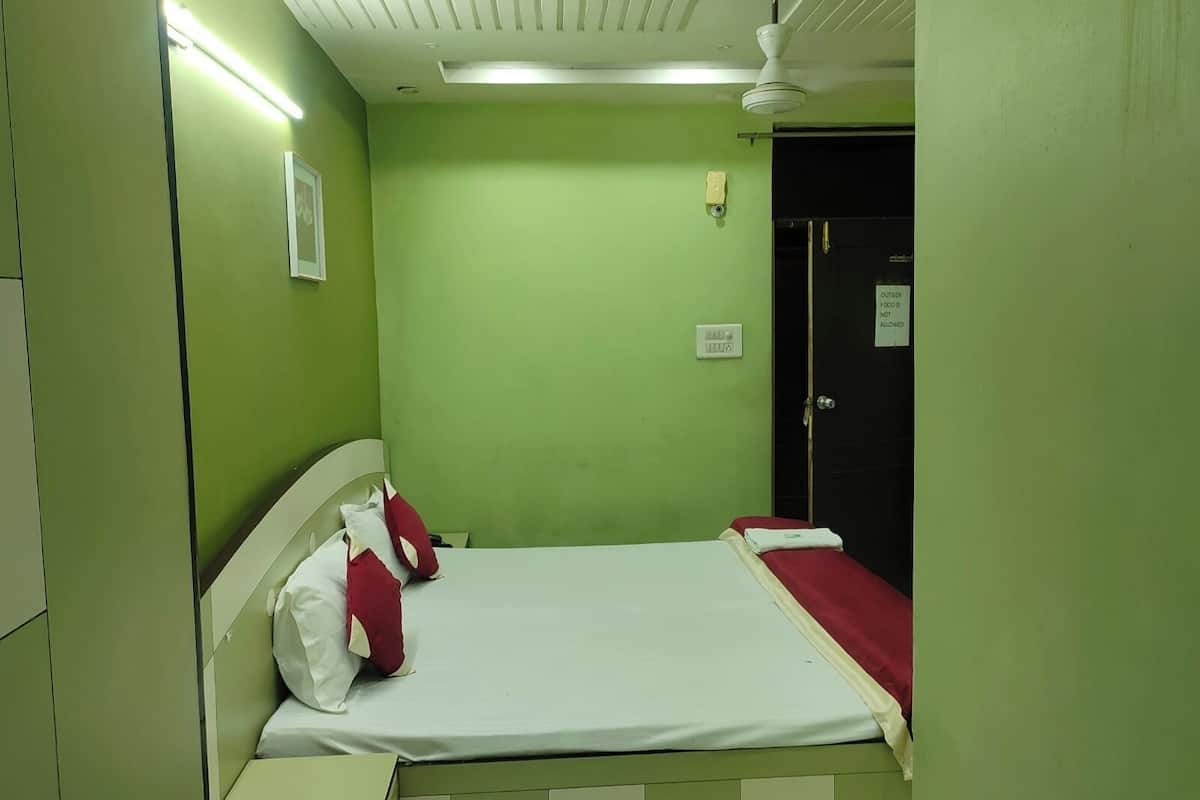 Una habitación pequeña con paredes verdes, una cama individual, un cabecero blanco y una manta roja.