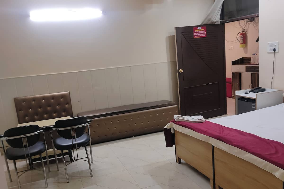 Habitación de hotel con cama, escritorio, dos sillas, banca y ventilador de techo.