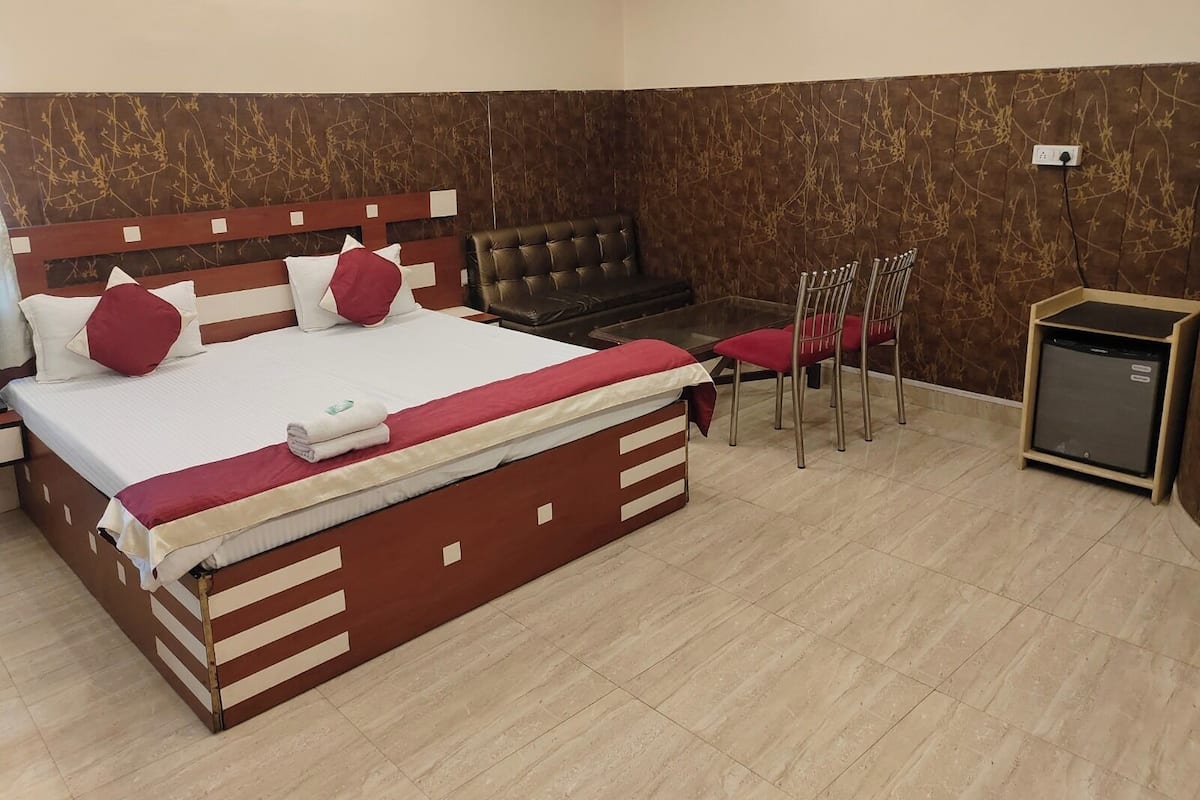 Una habitación de hotel con una cama grande, una mesita pequeña, un sofá y un refrigerador compacto.