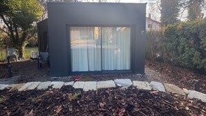 A modern, dark-colored building with large glass windows, surrounded by a stone border and a leaf-covered ground.
