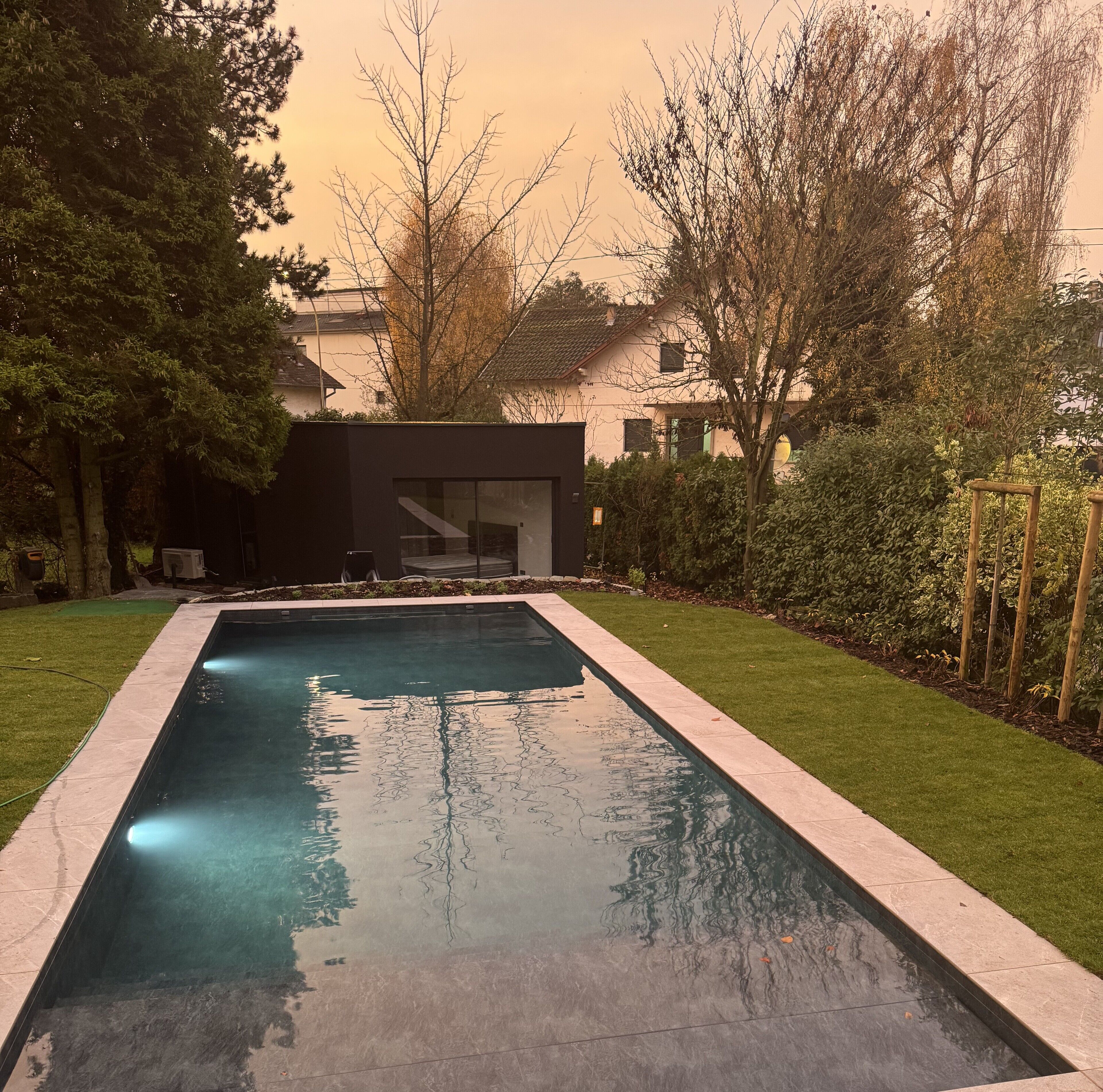 Une piscine rectangulaire à l’eau claire, entourée d’une pelouse bien entretenue et de divers arbres.