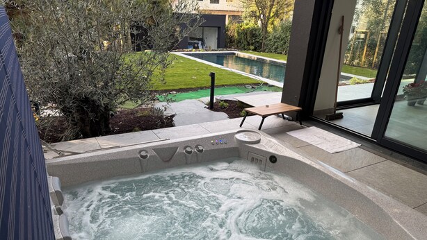 A hot tub with a view of a garden and a pool.