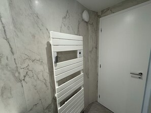 Une salle de bain avec un porte-serviettes blanc, une porte blanche et des murs en marbre.