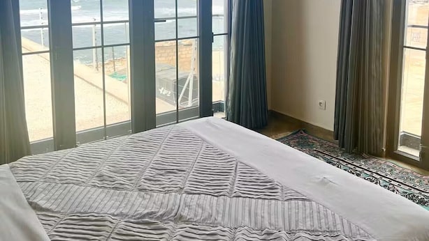 A bedroom with a large bed, a view of the ocean through floor-to-ceiling windows, and a balcony with a railing. - Residence Al Awane (Dakar)