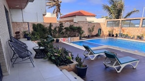 A pool area with lounge chairs, a small table, and potted plants. - Residence Al Awane (Dakar)