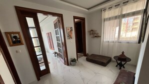 A spacious room with a tiled floor, a sofa, a small table, and a window with curtains. - Residence Al Awane (Dakar)