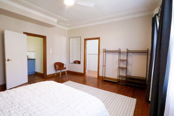 Un dormitorio con cama, una silla, armario, espejo y puerta que da a un baño.