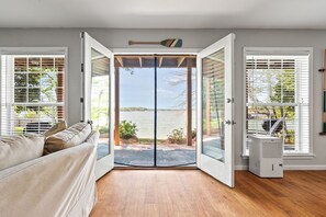 A room with a sliding glass door leading to an outdoor area, a white sofa, and a white air conditioning unit. - New! Daydream Believer is a 4BR, 2.5BA Lake Martin home that is PET FRIENDLY! (Dadeville)