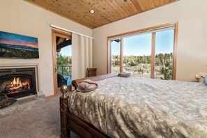 A bedroom with a fireplace, a large bed, and a view of a mountainous landscape through a sliding glass door. - Boulder Cove Lakefront Estate (Big Bear Lake)