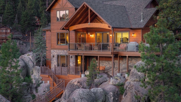 A multi-story log cabin with a balcony, surrounded by large rocks and trees. - Boulder Cove Lakefront Estate (Big Bear Lake)