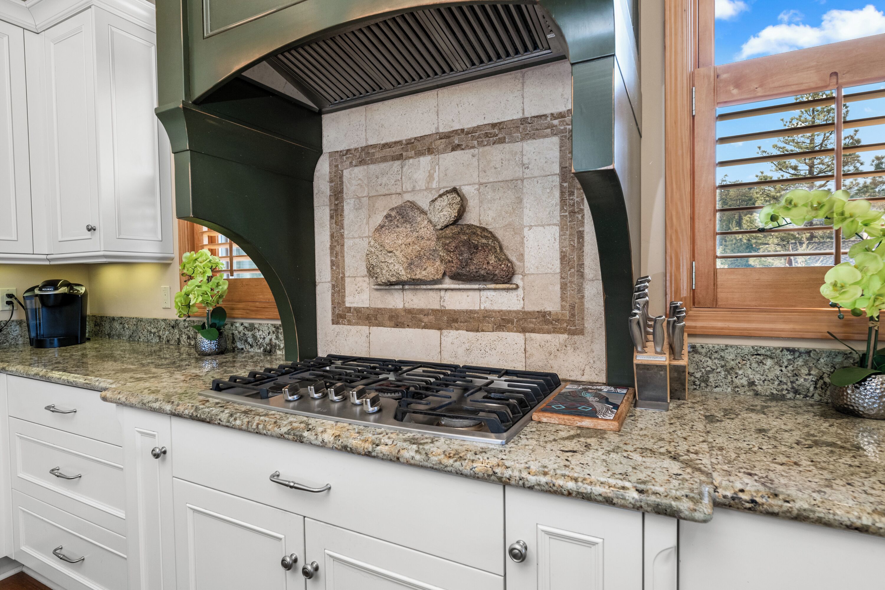A kitchen with granite countertops, white cabinetry, a gas stove, and a backsplash with a stone design.