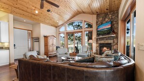A spacious living room with a large leather sectional sofa, a fireplace, and a stone accent wall. - Boulder Cove Lakefront Estate (Big Bear Lake)