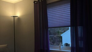 Een kamer met een bed, nachtkastje, vloerlamp en een raam met gordijnen.