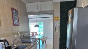Eine Küche mit einem Edelstahlkühlschrank, einem Toaster und einem Spülbecken. Durch einen offenen Durchgang ist ein Essbereich mit Tisch und Stühlen zu sehen.