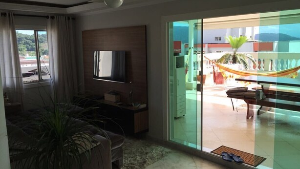 Ein modernes Wohnzimmer mit Flachbildfernseher, einer Couch und einer großen Schiebeglastür, die auf einen Balkon mit einer Hängematte führt.