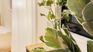 Een kamer met een bed, een grote potplant, een staande lamp en een televisie.