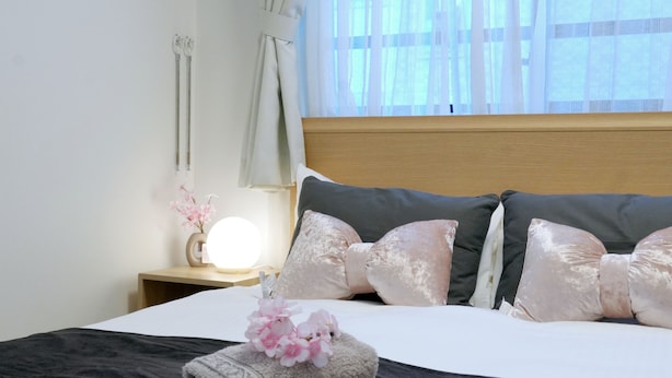 Een netjes opgemaakt bed met een zwart-wit dekbed, een houten hoofdbord en decoratieve kussens. Een nachtkastje met een lamp en een bloemenvaas is zichtbaar.