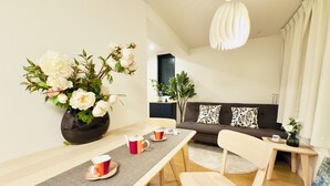 Een moderne woonkamer met een bank, een eettafel met stoelen, een bloemenvaas en een hanglamp.