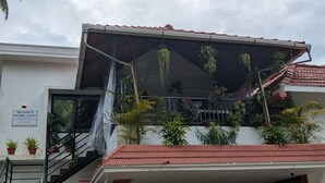 Un edificio de dos pisos con techo de tejas rojas, un balcón con plantas colgantes y un letrero que anuncia una casa de huéspedes.