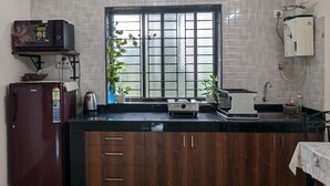 Una cocina con suelo de mármol, armarios de madera, microondas, refrigerador, lavamanos y ventana con vistas.