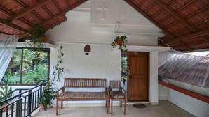 Un espacio al aire libre cubierto con un banco y sillas de madera, una puerta de madera y plantas en macetas.
