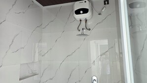 A bathroom with white marble tiles, a shower with a handheld showerhead, and a wall-mounted control panel. - Probosiwi Resort (Nanggulan)