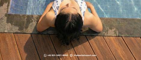 A person lying in a pool with tiled sides and a wooden deck.