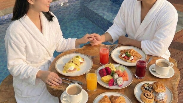 A couple dining by a poolside table with breakfast items, including eggs, fruit, and pastries. - Probosiwi Resort (Nanggulan)