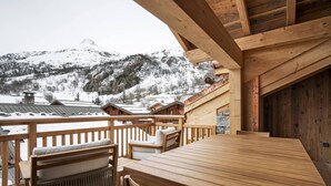 Eine Holzterrasse mit Tisch und Stühlen, mit Blick auf eine verschneite Berglandschaft.