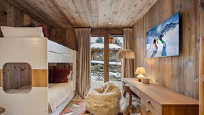 Ein gemütliches Zimmer mit Etagenbett, Schreibtisch, Stuhl und großem Fenster mit Blick auf eine verschneite Landschaft.