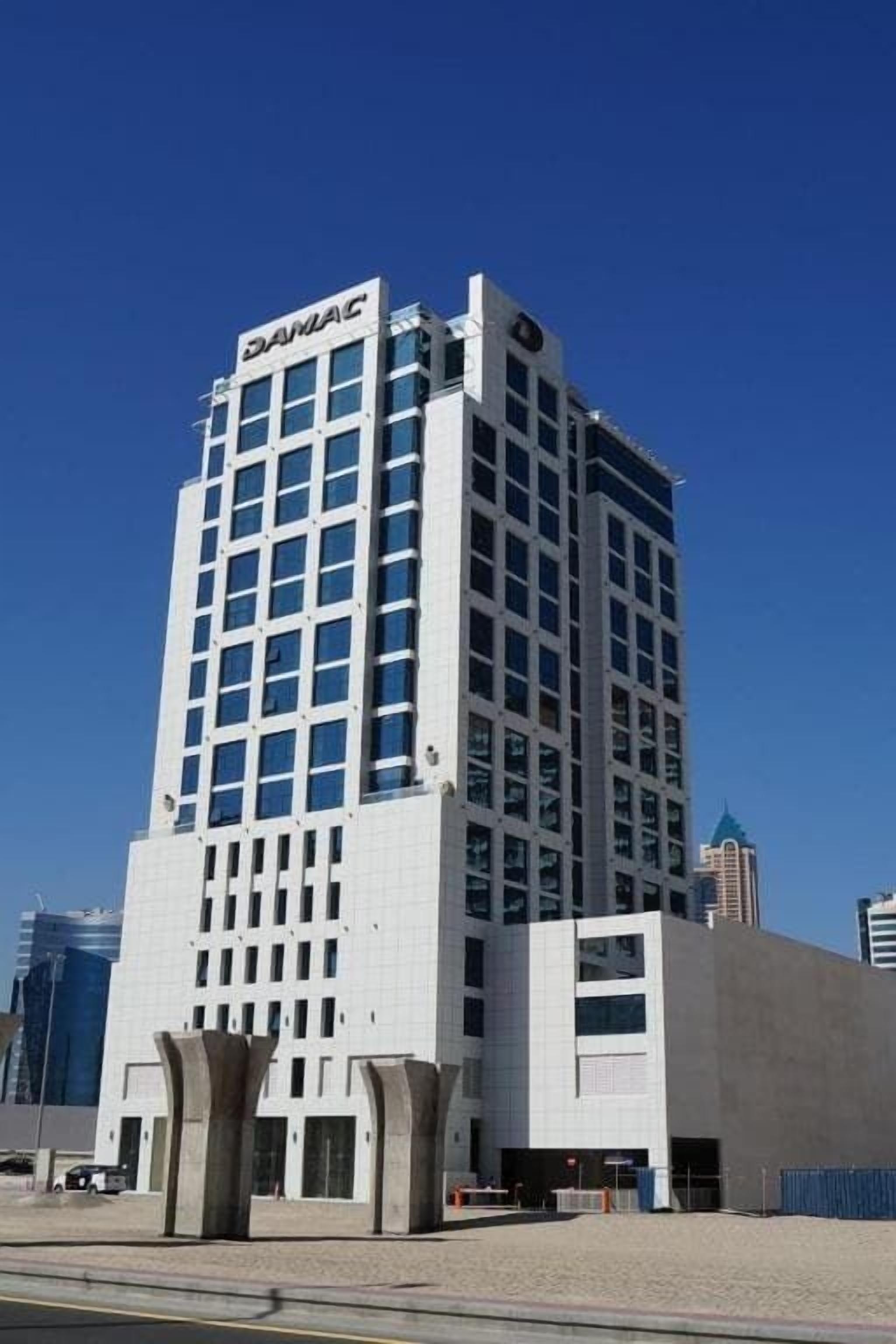 Un grand immeuble moderne, sur lequel on peut lire l’inscription « DAMAC » en haut.