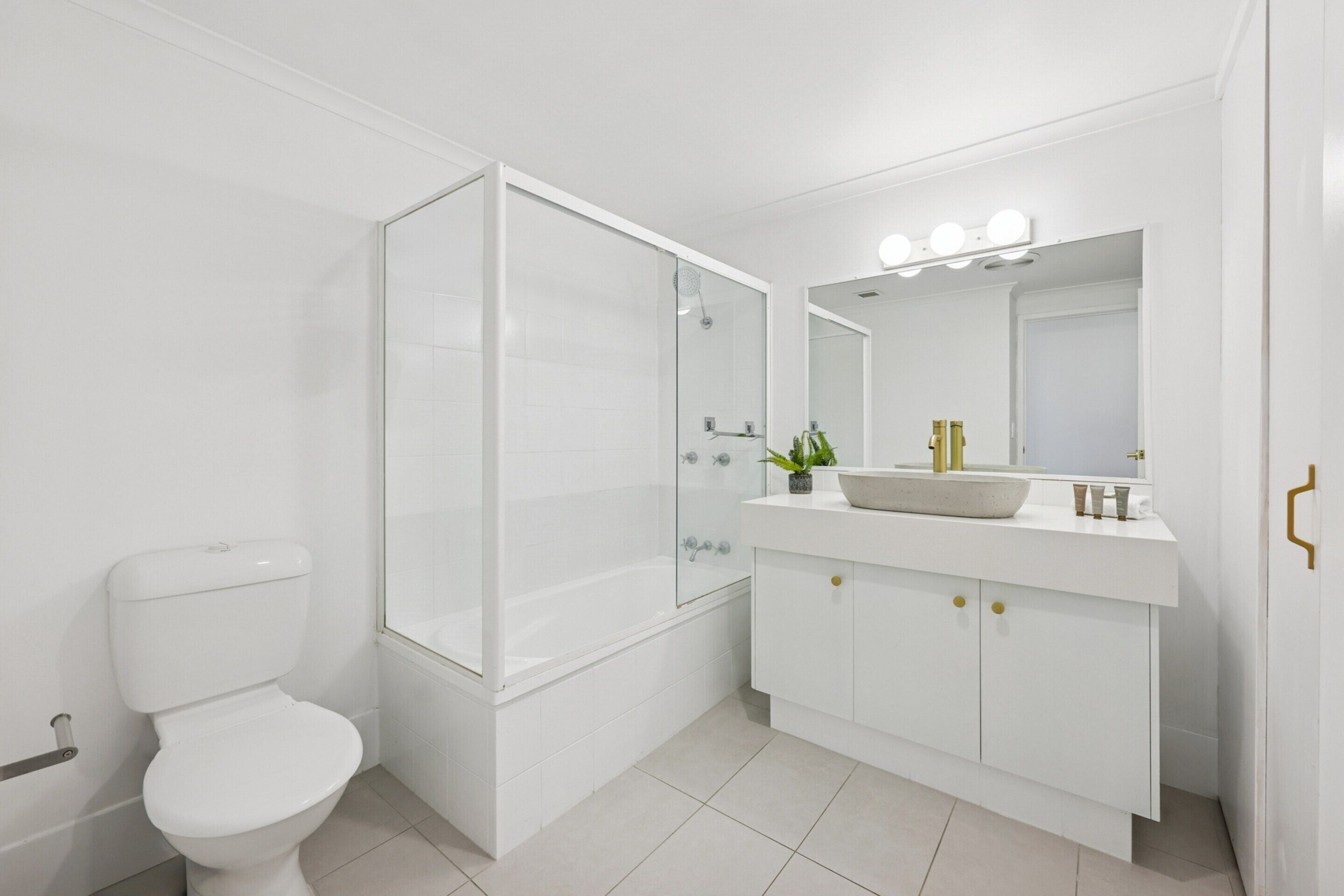 A modern bathroom with a toilet, a glass-enclosed shower, a vanity with a sink, and a mirror with lights.