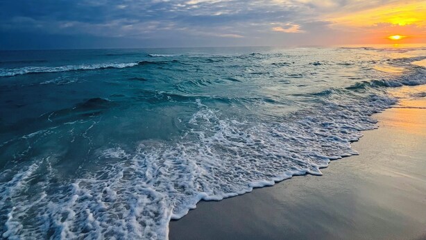 Une plage avec des vagues et un coucher de soleil.