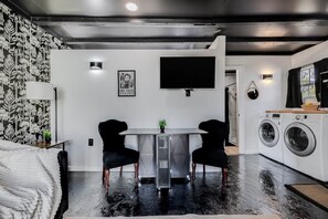 Una habitación moderna con una cama, un escritorio con dos sillas, un televisor, una lavadora y un papel tapiz estampado.