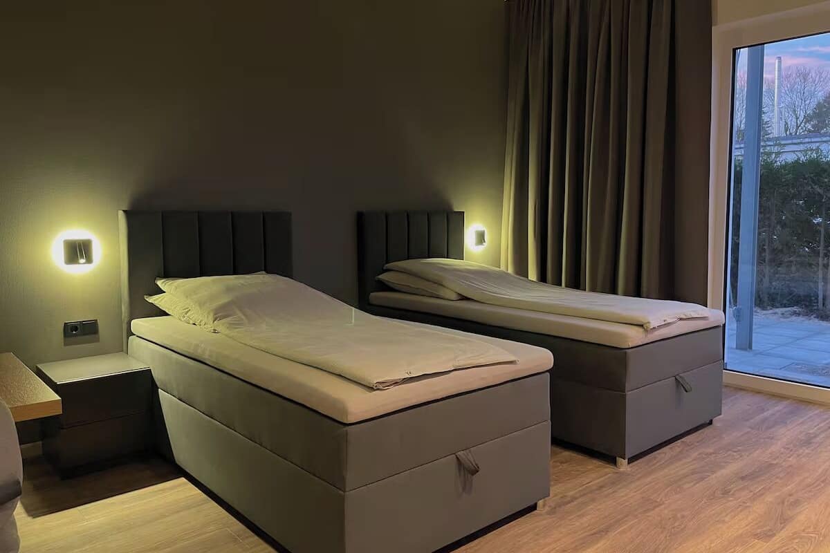 Una camera da letto moderna con due letti, comodini e un'ampia finestra con tende.