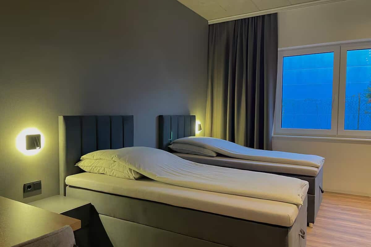 Una camera d'albergo con due letti, una scrivania e una finestra con tende.