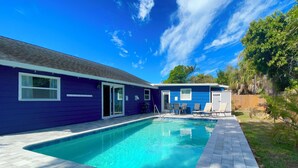 A swimming pool with a patio area, a covered seating area, and a house with a blue exterior. - Peaceful Oasis with Pool near Downtown and Beaches (Sarasota)