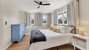 A bedroom with a bed, a nightstand, a dresser, a ceiling fan, and windows with curtains. - Peaceful Oasis with Pool near Downtown and Beaches (Sarasota)
