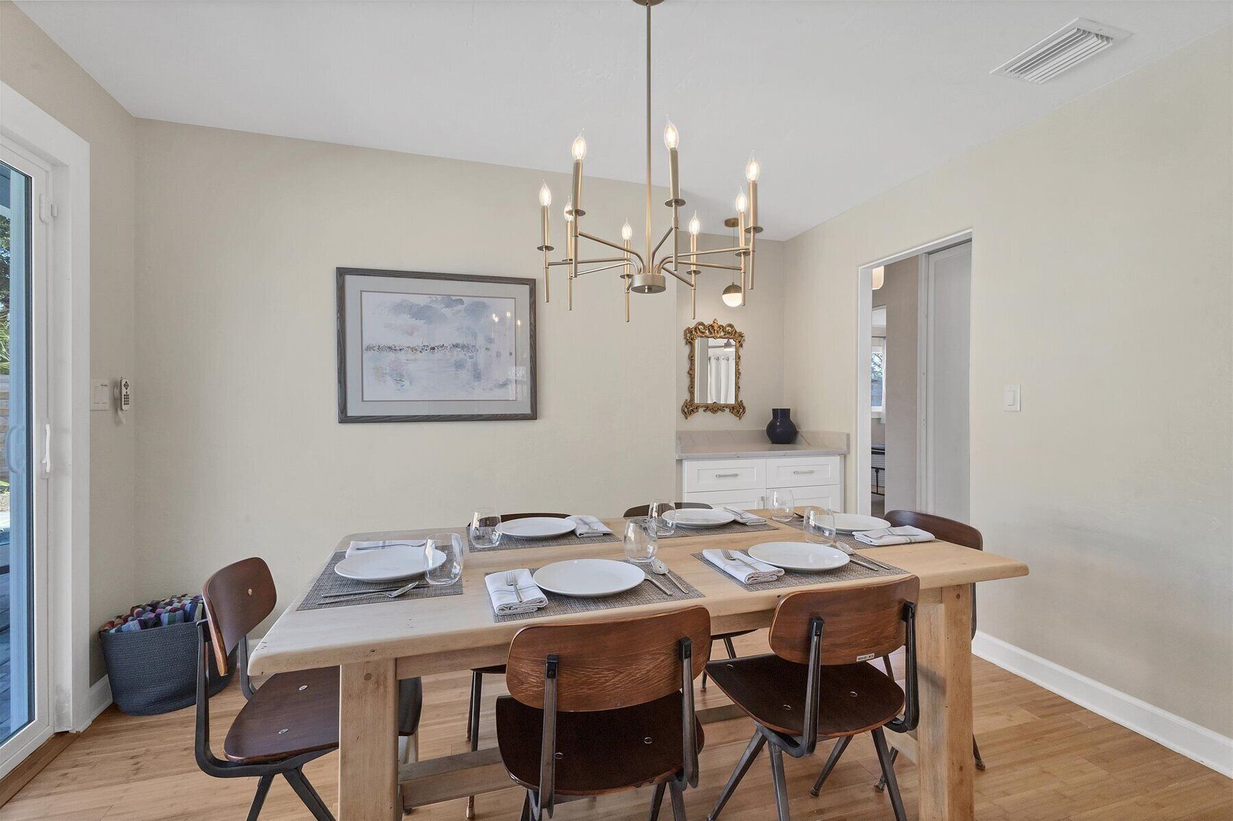 A dining area with a table set for four, a chandelier, and a framed picture on the wall.