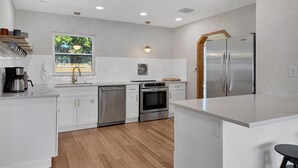 A modern kitchen with white cabinets, stainless steel appliances, and a wooden floor. - Peaceful Oasis with Pool near Downtown and Beaches (Sarasota)