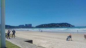A beach with people walking and a bicycle. There are buildings in the background. - Vacation home in Guarujá. (Guarujá)