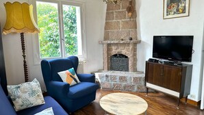 Ein Wohnzimmer mit einem blauen Sofa, einem runden Couchtisch, einem Kamin aus Stein, einem Fernseher auf einer Holzeinrichtung und einer Lampe.