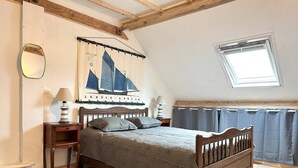 Ein Schlafzimmer mit einem hölzernen Bett, einem Nachttisch, einer Lampe, einem Spiegel, einem Fenster mit Vorhängen und einer Wand mit einem Poster von einem Segelboot.
