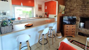 A modern kitchen with a central island, white bar stools, a stone fireplace, and a television. - Beachfront house in Trébeurden with garden and terrace (Trébeurden)