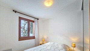 Makuuhuoneessa on sänky, kaksi yöpöytälamppua, ikkuna, josta on näkymä puita kohti, ja puinen tuoli.